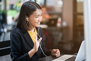 Young woman wearing headphones smiles at her laptop in a cafe