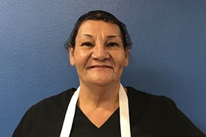 Smiling woman with short dark hair in a black top and white lanyard poses against a blue wall.
