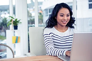 Smiling woman wearing a striped shirt using a laptop at a bright desk