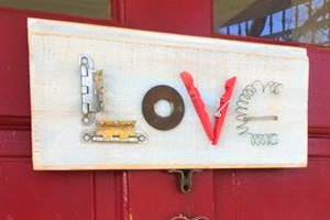 Decorative LOVE sign made from scrap metal parts on a white weathered board against a red door.