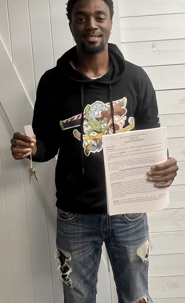 Man in a black hoodie holds keys in one hand and documents in the other indoors.