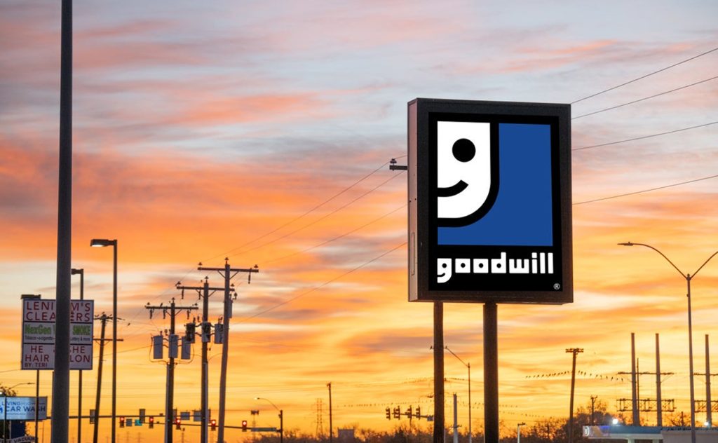 Goodwill sign on a pole against a vivid sunset sky over an urban street.
