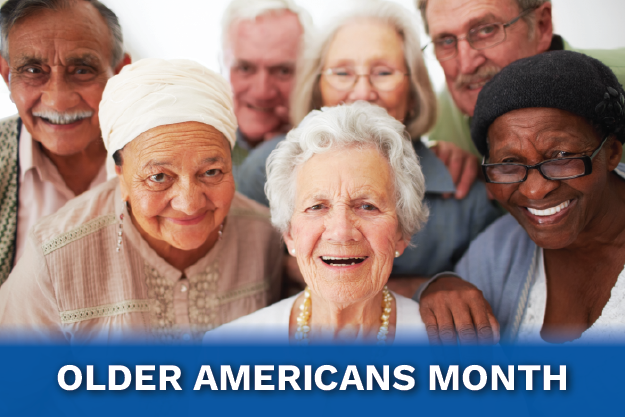 Smiling diverse group of elderly adults posing for a group photo with a blue banner reading Older Americans Month.