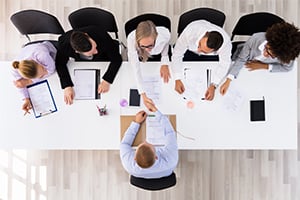 Overhead view of diverse professionals around a conference table collaborating with papers, tablets, and smartphones.