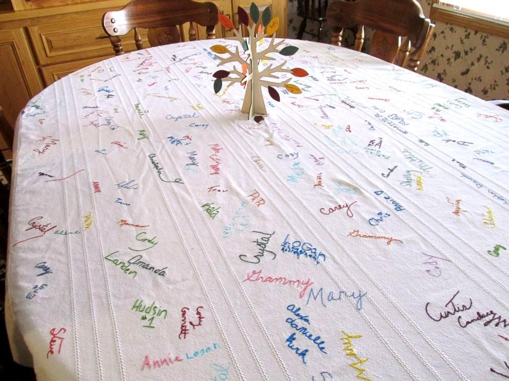 Round dining table with a white signature tablecloth and a paper tree centerpiece in a wood-paneled dining room.