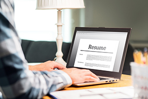Person typing on a laptop with a resume displayed on screen at a tidy desk with a lamp.