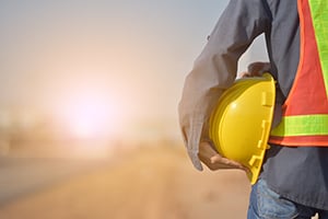 Construction worker with hi-vis vest holding a yellow hard hat at sunset