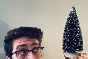 Person with glasses looks up at a tall black cone-shaped object dusted with snow against a beige wall.