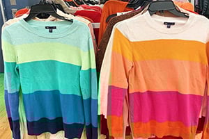 Colorful striped knit sweaters on a clothing rack.
