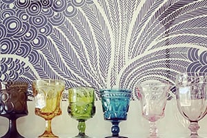 Row of colorful glass goblets in front of a purple and white swirling wallpaper