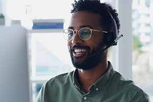 Smiling man with headset and glasses working at a computer in a bright office.