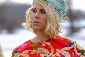 Woman with blonde hair wearing a turquoise headwrap and a red floral top, outdoors in a snowy landscape.