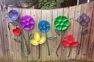 Colorful metal flower sculptures mounted on a weathered wooden fence in a cheerful garden.