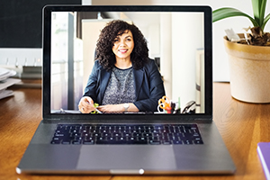 Professional woman with curly hair on a video call, displayed on a laptop screen at a desk.