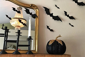 Mantel display with a gold-framed mirror, black candle holders, a glittery black pumpkin, and bat silhouettes on the wall.