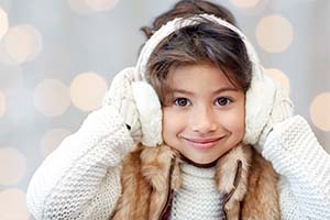 Smiling young girl wearing white earmuffs and a knit sweater with a fur vest.