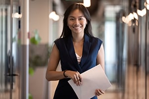Professional woman in hallway holding documents, smiling at the camera.