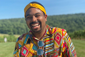 Smiling man wearing a colorful geometric shirt and yellow headband outdoors.