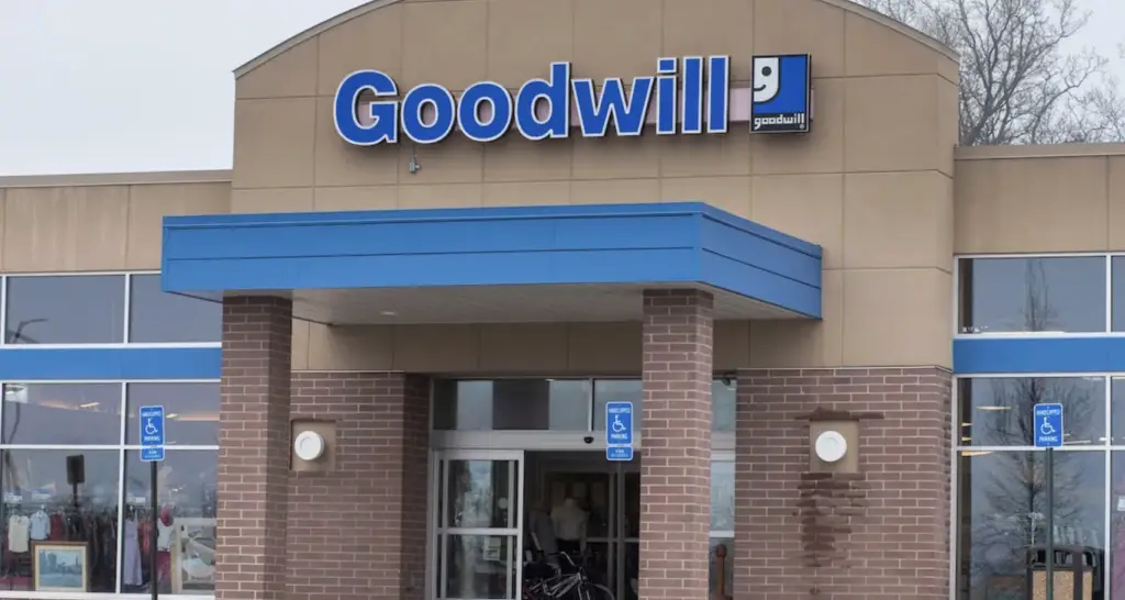 Front view of a Goodwill store entrance with a blue awning, brick pillars, and wheelchair parking signs.