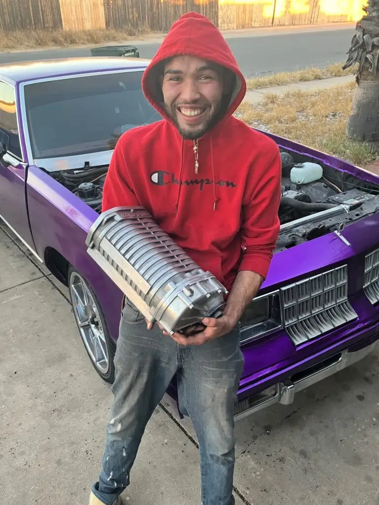 A picture of a man wearing a red hood standing in front of a purple car