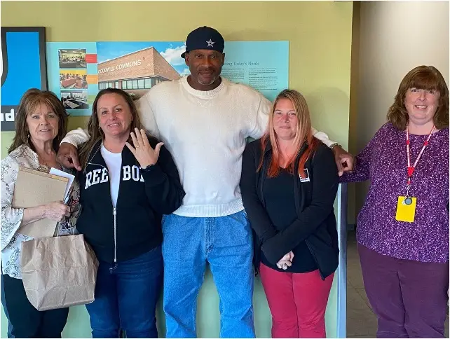 A picture of a group of 5 people standing in front of a poster of a building