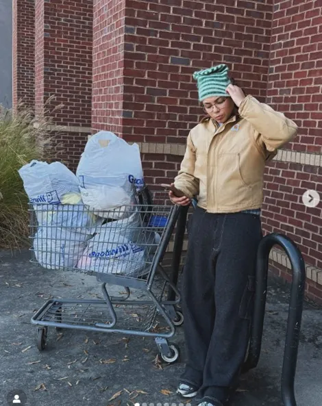 Women wearing a bege jacket and green hat pushing a cart full of bags 